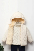 A cream-colored children's puffer jacket with a soft fleece-lined hood and collar, styled over a cream cable-knit turtleneck sweater and dark pants, hanging on a white wall, Obroi
