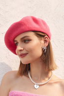 Woman wearing a pink beret and pearl necklace against a light background, Obroi