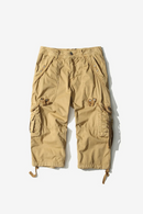 A pair of tan cargo pants with multiple utility pockets and drawstring leg cuffs, laid flat against a light off-white background, Obroi