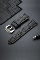 Black leather watch strap with silver buckle on a dark surface, Obroi